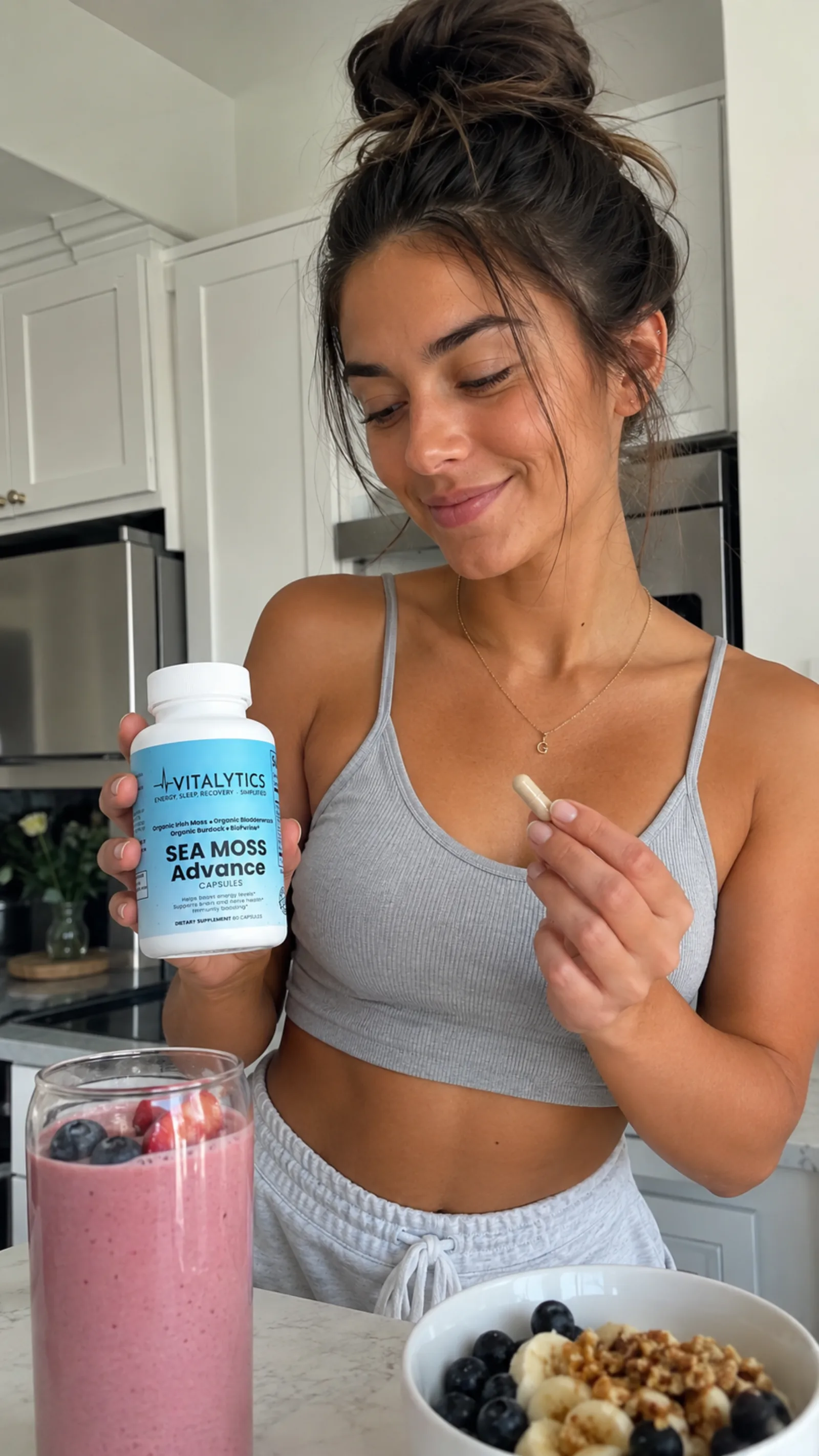 Woman holding a Vitalytics bottle and capsule beside a pink smoothie and fruit bowl.